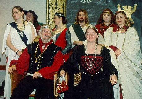 At Twelfth Night Coronation XXXIV/2000. Accompanied by: (L to R, behind the thrones) Optia (Sgt.) Vesta Antonia Aurelia (Defender of the Summits), Lord Lucian MacCrimmon (Summits Captain of Cats), Magistra Raven Qara ton (Cup Bearer), Sgt. Bannor Oldenmoor, Bantierna (Lady) Grainne Gelleo of Locksley, Charlotte Nicholls. (Our thanks to Finngall McKetterick for providing the names of the retinue.)