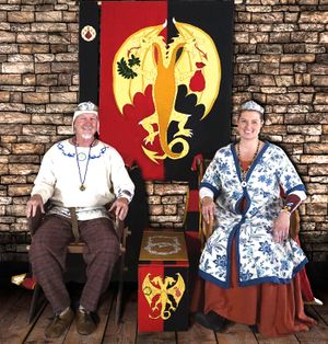 Arion and Kloe sitting in garb in front of the Baronial banner facing the viewer