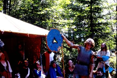 An Tir Coronet Tourney 17, May 12-13, 1979. Torgul being awarded the Shattered Shield. Prince Manfred and Princess Koressa (seated on the left) of An Tir. Trelon and Tamsin, as the next heirs, are sitting on the right side with wreaths on their heads. Sir Seamus Peacemaker is standing on the right. Photo courtesy of Rowena de Manning.